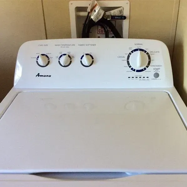 Control panel and lid of a white Amana top-load washer in a laundry room