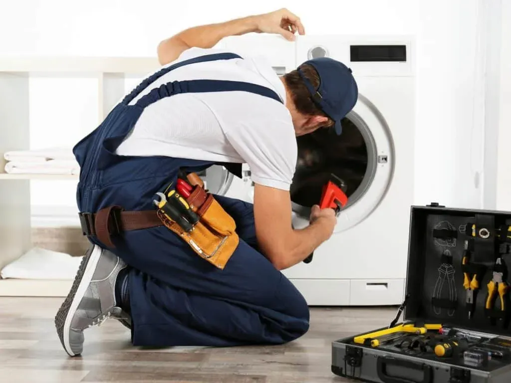 Technician with a tool belt fixing a front-load washer with a wrench