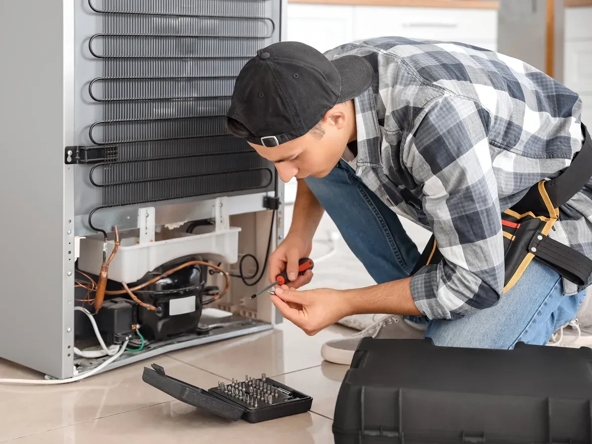 Technician wiring a refrigerator compressor with the condenser coils exposed