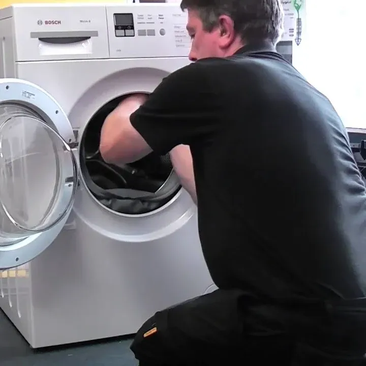 Technician reaching into the drum of a Bosch front-load washer with the door open