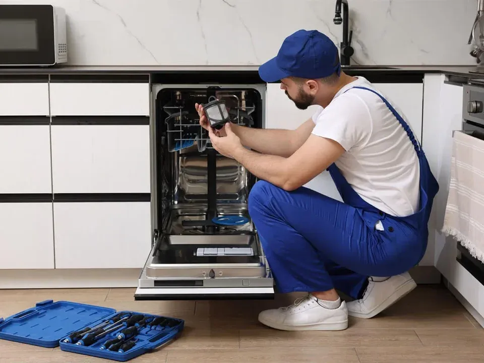 Technician inspecting a dishwasher filter, with a toolbox on the kitchen floor
