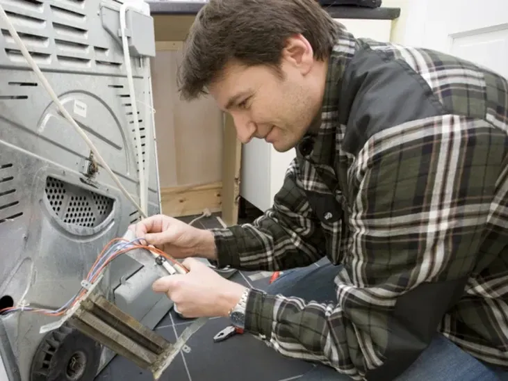 Technician working on the heating element at the back of an electric dryer
