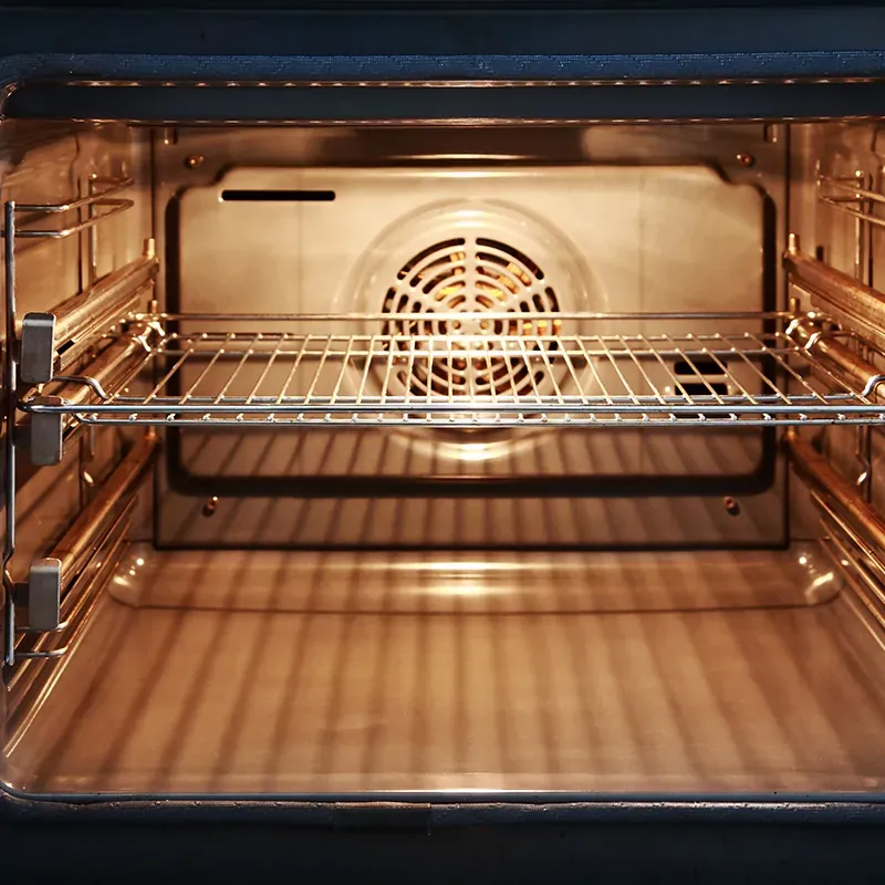 Inside of an empty convection oven with the light on, a wire rack and the rear fan cover