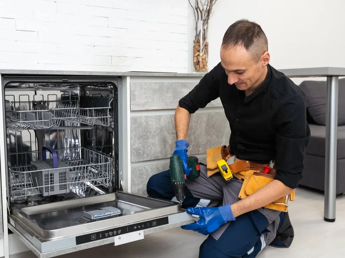 Technician in blue gloves drilling the door of a built-in dishwasher