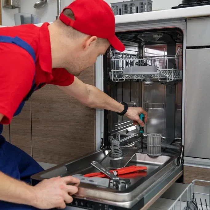 Technician in a red cap using a screwdriver inside an open dishwasher