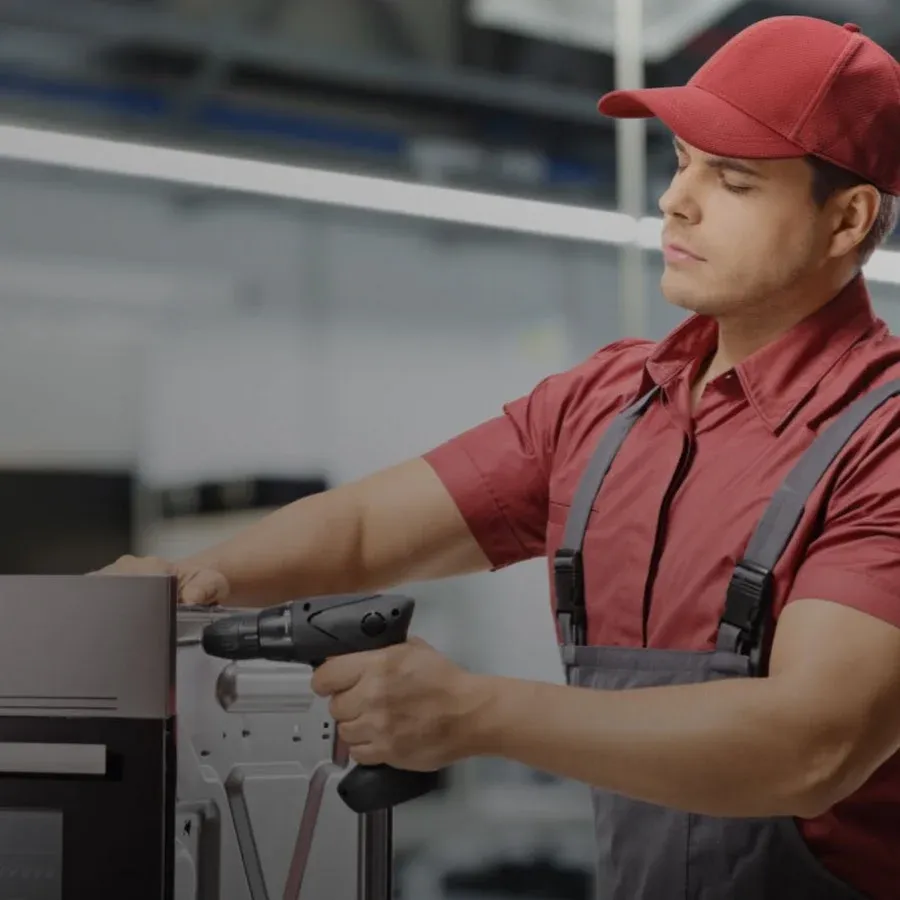 Appliance technician in a red cap using a cordless drill to service a built-in oven