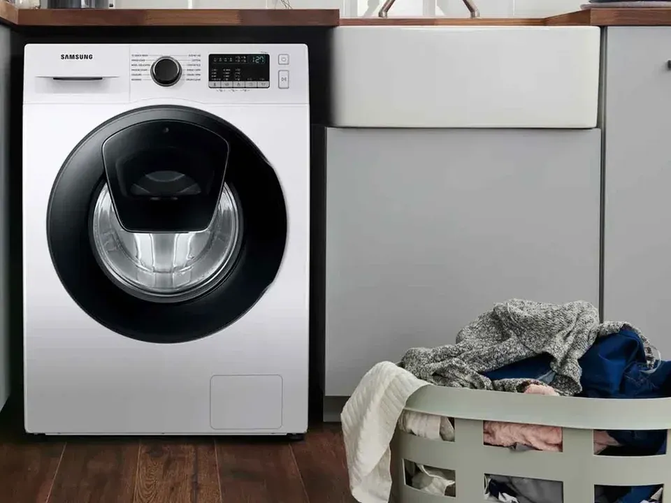 White Samsung front-load washer beside a basket of laundry in a home laundry room